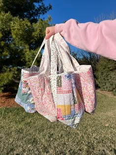 a person holding two bags in their hand on the grass with trees in the background