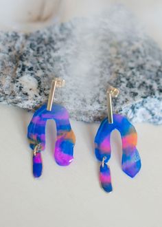 two pairs of colorful earrings sitting on top of a white table next to a rock