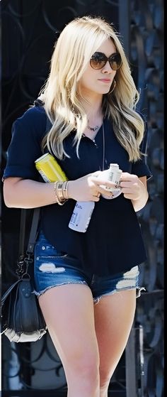 a woman in short shorts is looking at her cell phone while walking down the street