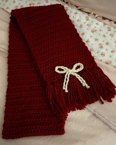 a red knitted scarf with a white bow on it's end laying on a bed