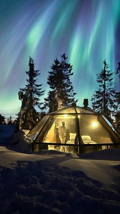 a person standing in front of a tent under the aurora bore, with trees and snow