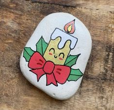 a painted rock with a candle and holly leaves on it sitting on a wooden surface