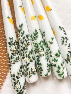 five white candles with yellow flowers and leaves on them