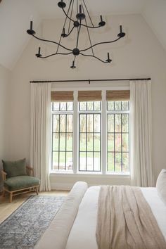 a bed sitting under a window next to a white curtained wall in a bedroom