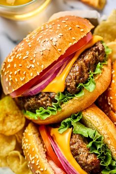 two hamburgers with lettuce, tomato and onion on them next to potato chips