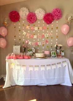 a table topped with pink and white balloons next to a wall covered in paper pom poms