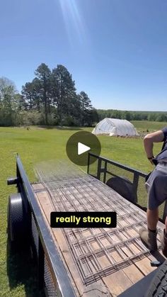 a man sitting on the back of a truck in front of a field with trees