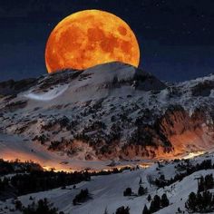 the full moon rising over mountains with snow on them