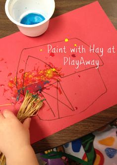 a child's hand is painting on a playmat with paint and straws