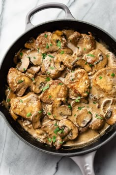 a skillet filled with chicken and mushrooms covered in gravy on top of a marble counter