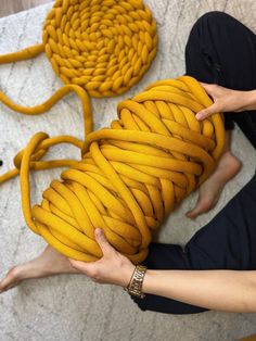 a woman is holding a yellow rope on the floor next to some other items that have been made out of yarn