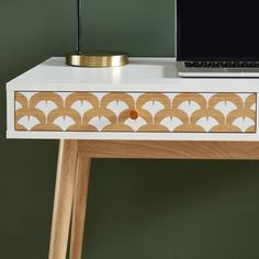 a laptop computer sitting on top of a wooden desk next to a white table with gold trim