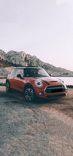 a small red car parked in front of a body of water