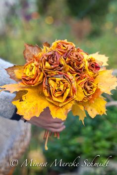 a woman holding a bouquet of yellow and red flowers in her hands with leaves on it