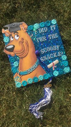 a graduation cap and tassel laying on the grass with an image of scooby