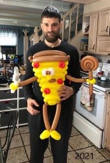 a man standing in a kitchen holding a balloon shaped like a pizza