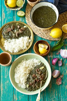 two bowls filled with white rice and spinach stew next to some lemons, garlic, and lime wedges