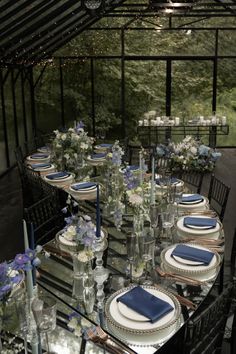 a table set up with blue and white place settings for an outdoor dinner party in a greenhouse