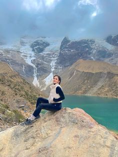 a woman sitting on top of a rock next to a lake