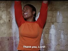 a woman in an orange and black shirt is holding her arms above her head with the words thank you lord