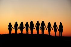 a group of people holding hands while standing on top of a hill at sunset or dawn