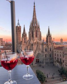 two wine glasses sitting on top of a wooden table next to a tall building with spires