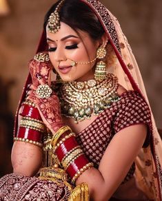 a woman in red and gold bridal outfit holding her hands to her face while looking at the camera