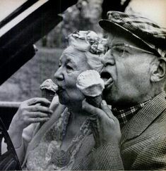 an old man and woman are eating something off of their mouths as they stand next to each other