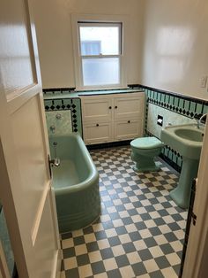 a bathroom with checkered floor and green bathtub next to sink, toilet and window