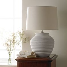 a white lamp sitting on top of a wooden table next to a book and vase