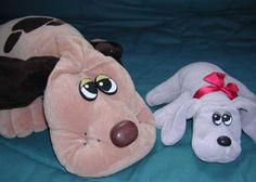 two stuffed animals laying next to each other on a blue surface with one dog wearing a red bow