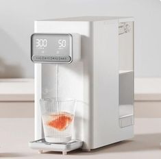 a white water dispenser sitting on top of a counter next to a glass filled with liquid