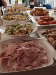 a table filled with different types of food on white plates and serving utensils