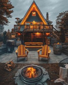 a fire pit sitting in front of a house with two chairs around it and lights on