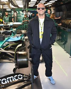 a man standing next to a racing car in a garage with other people behind him