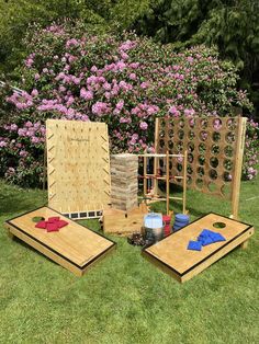 two cornhole boards and some pieces of wood on the grass with purple flowers in the background