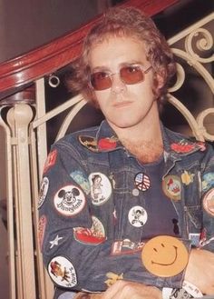 a man with sunglasses on sitting in a chair holding an orange smiley face brooch