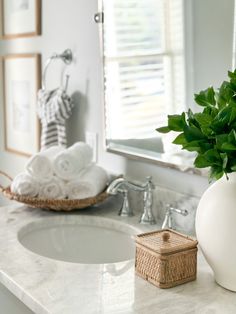 a bathroom sink with a white vase filled with green leaves on top of it next to a mirror