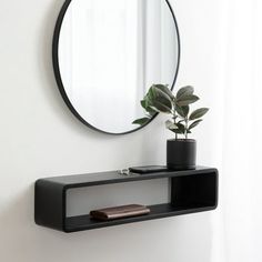 a round mirror on the wall above a shelf with a potted plant