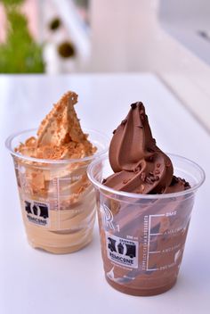 two plastic cups filled with different types of desserts on top of a white table