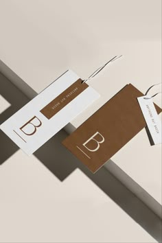 two brown and white business cards hanging from a metal bar with the letter b on it