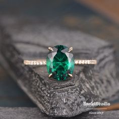 an emerald colored ring with diamond accents on the band and in front of a rock