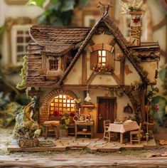 a doll house with a table and chairs in front of it, surrounded by greenery