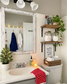 a white toilet sitting under a bathroom mirror next to a christmas tree and potted plant