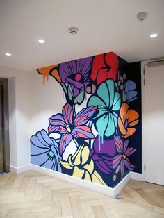 a large colorful painting on the side of a wall in an empty room with hard wood flooring