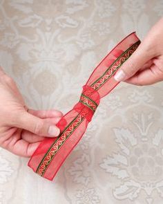 two hands are holding a red ribbon on a white tablecloth with floral designs and gold trimmings