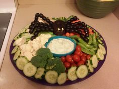 a purple plate topped with lots of vegetables and fruit next to a bowl of dip