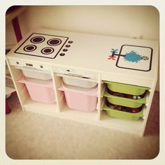 a toy stove top oven sitting on top of a white shelf with bins underneath it