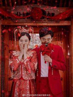 a man and woman standing next to each other in front of a doorway with red flowers