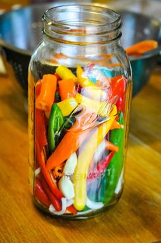 a glass jar filled with lots of different colored peppers on top of a wooden table